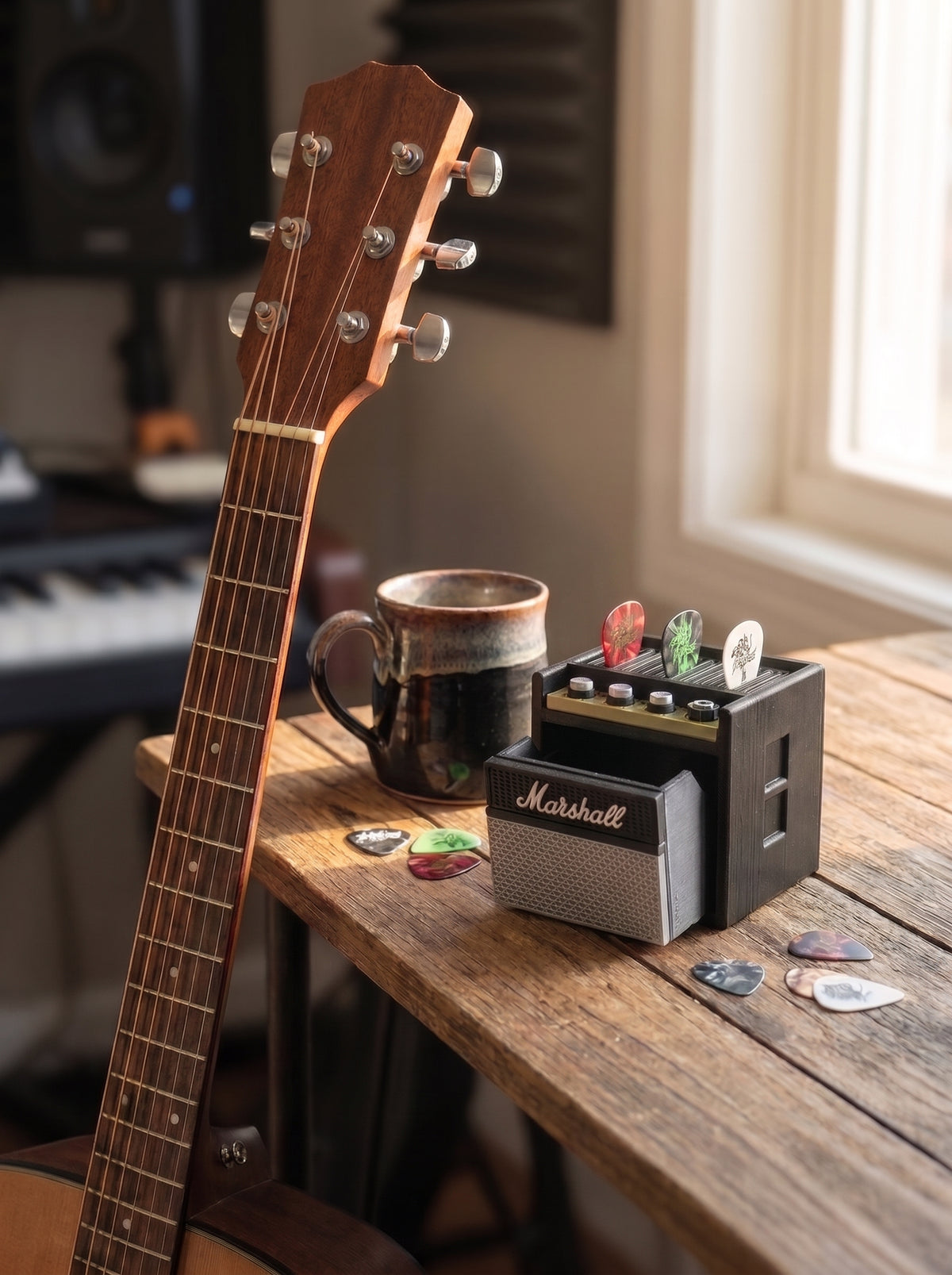 Mini guitar amp holding picks on a wooden desk next to an acoustic guitar