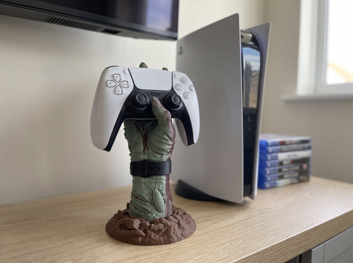 Zombie hand controller holder holding a white PS5 controller on a TV unit beside a games console